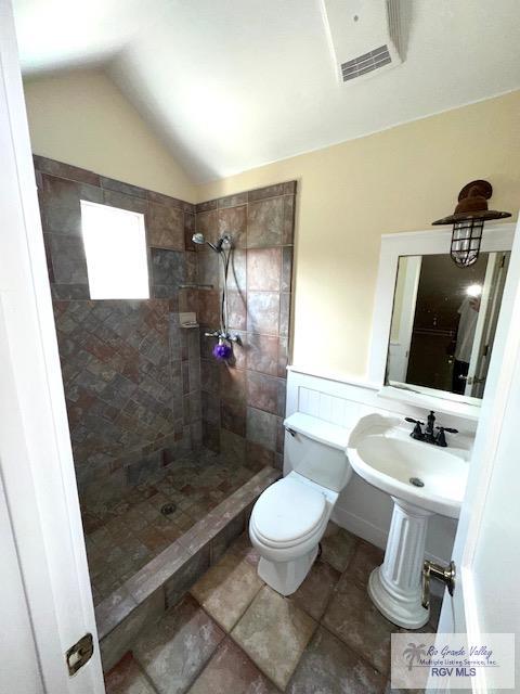 bathroom with a tile shower, lofted ceiling, and toilet