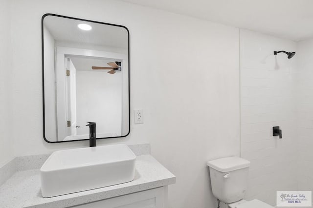 bathroom with vanity, tiled shower, ceiling fan, and toilet