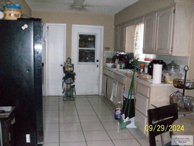 kitchen with tile counters, white cabinetry, black fridge, and light tile patterned floors