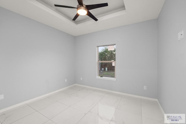 empty room with marble finish floor, ceiling fan, a raised ceiling, and baseboards