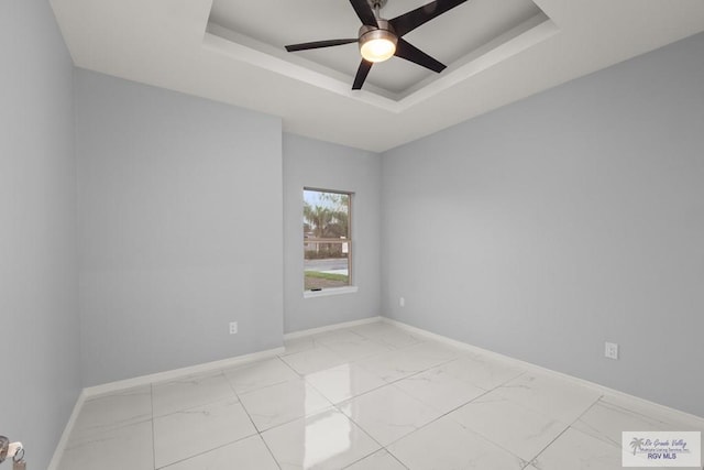 spare room with baseboards, a raised ceiling, marble finish floor, and a ceiling fan