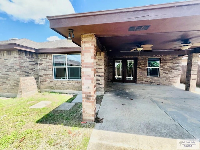 entrance to property featuring ceiling fan, a patio area, and a lawn