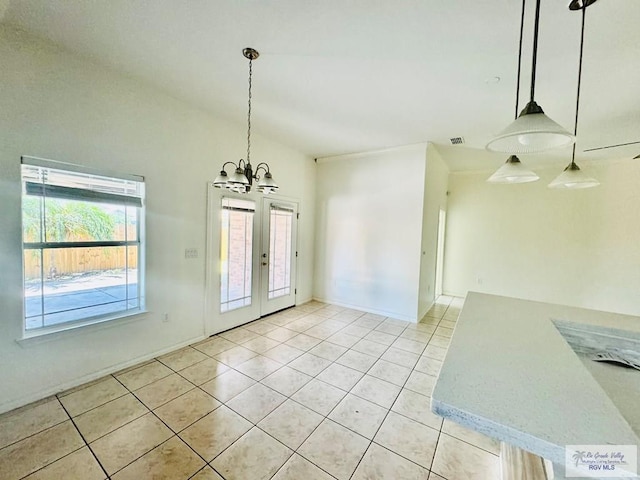 unfurnished dining area with a notable chandelier, light tile patterned flooring, and french doors