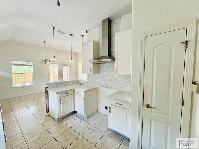 kitchen featuring backsplash, white cabinets, wall chimney exhaust hood, decorative light fixtures, and kitchen peninsula