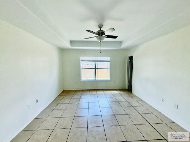 tiled spare room featuring a raised ceiling and ceiling fan