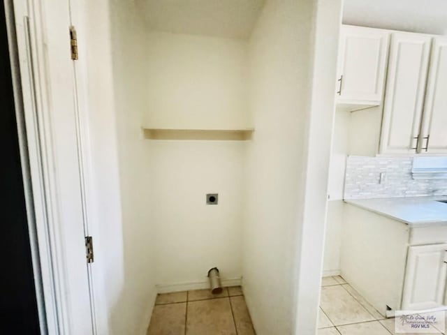 washroom with electric dryer hookup, light tile patterned floors, and cabinets