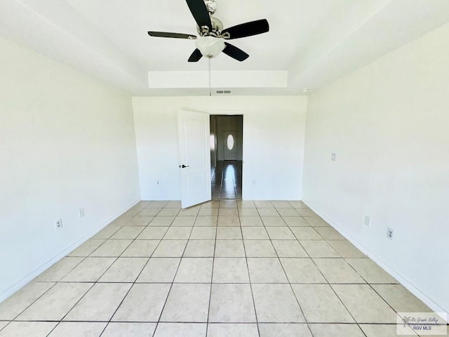 spare room featuring a tray ceiling, ceiling fan, and light tile patterned floors