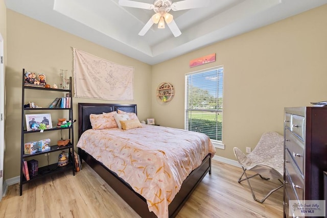 bedroom with a ceiling fan, a raised ceiling, light wood-style flooring, and baseboards