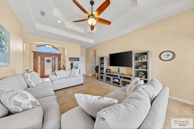 living area with light tile patterned floors, visible vents, a ceiling fan, baseboards, and a tray ceiling