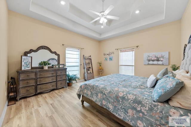 bedroom with wood finished floors, multiple windows, a raised ceiling, and recessed lighting