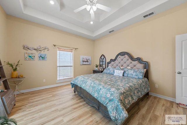 bedroom featuring wood finished floors, a raised ceiling, visible vents, and baseboards