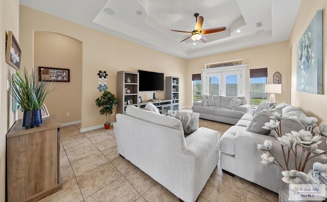 living room featuring baseboards, visible vents, a tray ceiling, and arched walkways