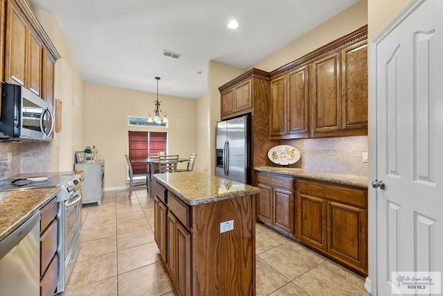 kitchen with light tile patterned floors, appliances with stainless steel finishes, a kitchen island, and brown cabinets