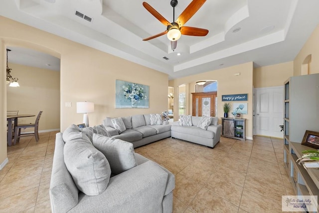 living room featuring arched walkways, light tile patterned floors, ceiling fan with notable chandelier, visible vents, and a raised ceiling