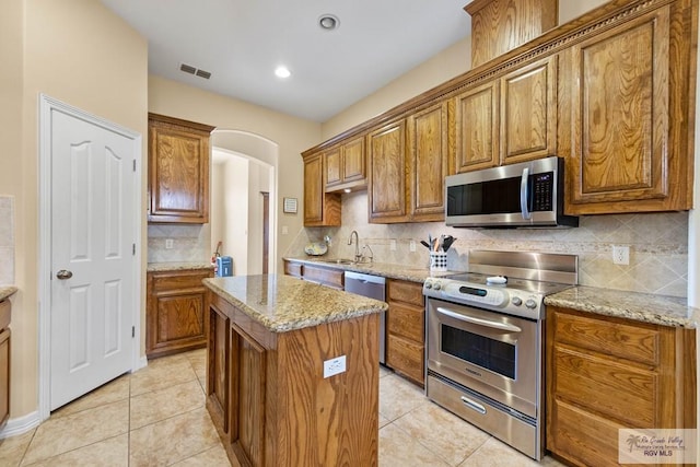 kitchen featuring arched walkways, stainless steel appliances, a kitchen island, visible vents, and brown cabinetry