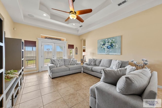 living area with visible vents, ceiling fan, a tray ceiling, french doors, and light tile patterned flooring