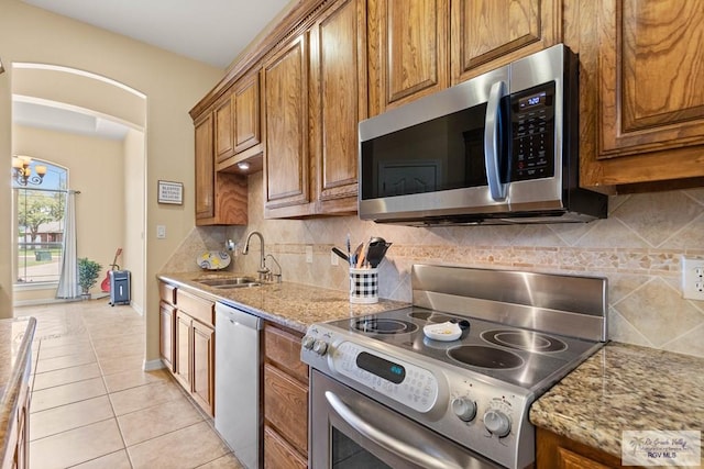 kitchen featuring brown cabinets, backsplash, appliances with stainless steel finishes, light tile patterned flooring, and a sink