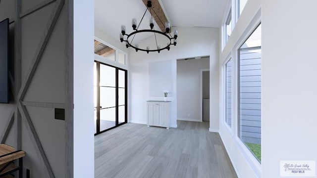 hallway featuring beam ceiling, light wood finished floors, a high ceiling, a chandelier, and baseboards