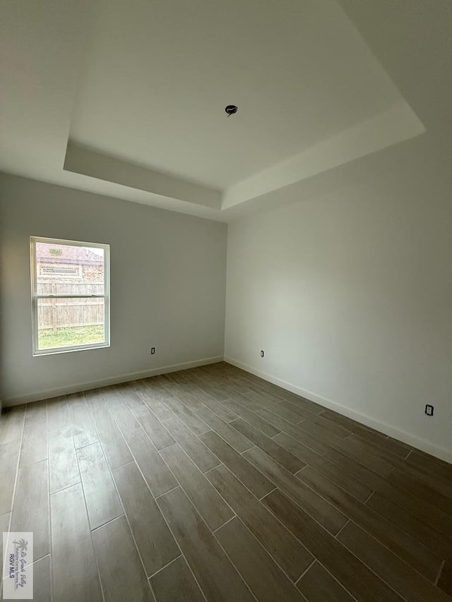 empty room featuring dark wood-style floors, a raised ceiling, and baseboards