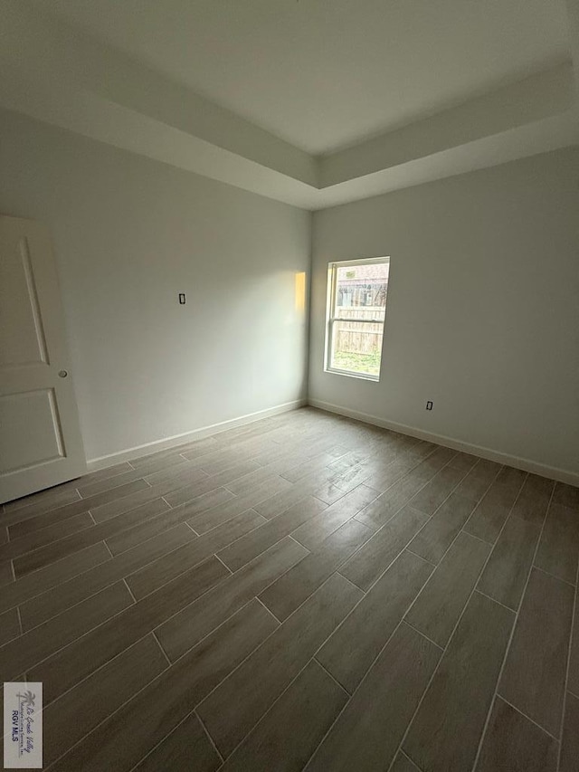 empty room featuring baseboards, a raised ceiling, and wood finish floors