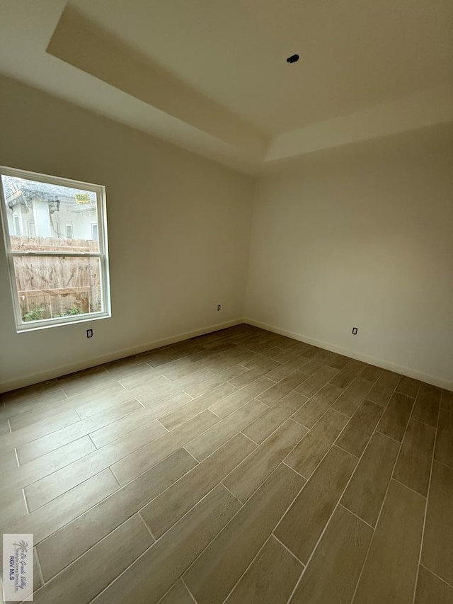 empty room featuring baseboards, a tray ceiling, and wood finish floors