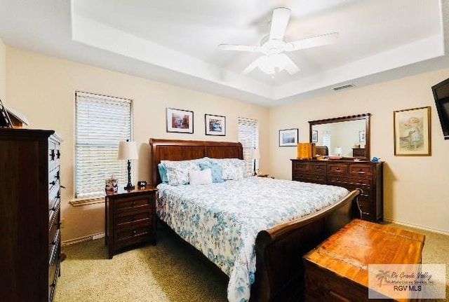 bedroom with ceiling fan, light colored carpet, and a tray ceiling