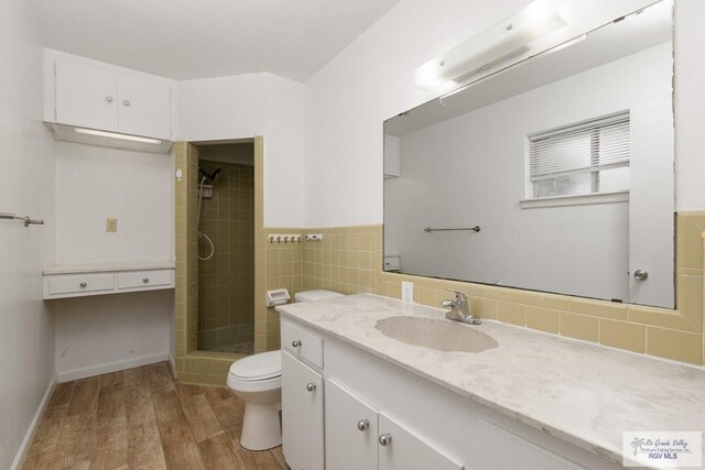 bathroom featuring a tile shower, vanity, wood-type flooring, and toilet