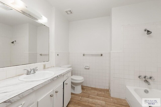 full bathroom with vanity, wood-type flooring, tile walls, toilet, and tiled shower / bath