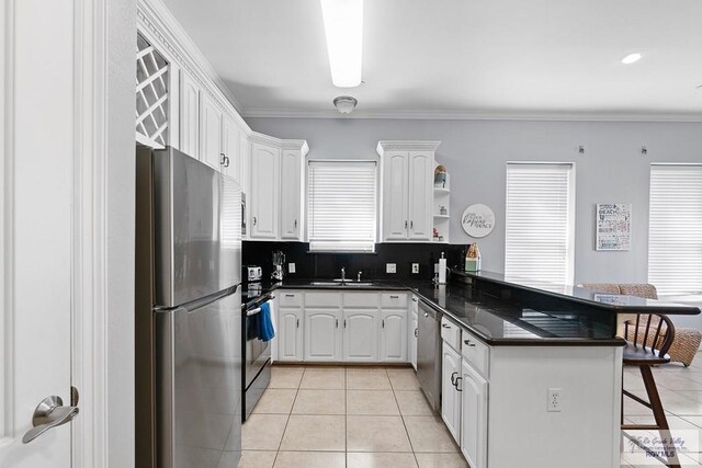 131 E Saturn Ln, South Padre Island, TX 78597 - kitchen with appliances with stainless steel finishes, a peninsula, dark countertops, a breakfast bar, and light tile patterned floors
