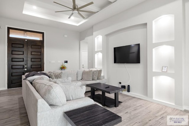 living room featuring a tray ceiling, ceiling fan, and light wood-type flooring