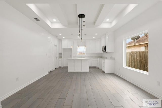 kitchen with light wood-type flooring, a tray ceiling, a center island, white cabinetry, and hanging light fixtures