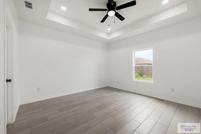 unfurnished room featuring a tray ceiling, ceiling fan, and hardwood / wood-style floors