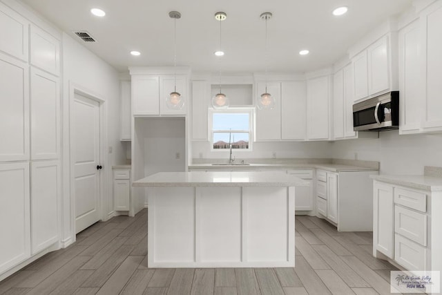 kitchen with white cabinetry, sink, a kitchen island, and decorative light fixtures