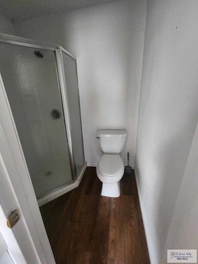 bathroom with a shower stall, toilet, and wood finished floors