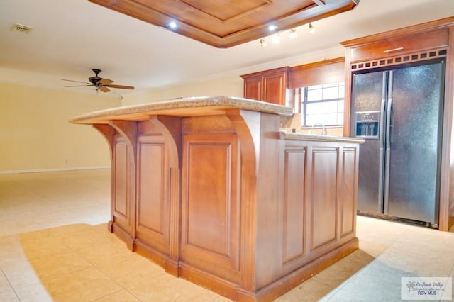 kitchen with black refrigerator with ice dispenser, a raised ceiling, ceiling fan, ornamental molding, and a kitchen island