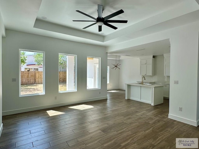 unfurnished living room featuring a tray ceiling, a sink, dark wood-style floors, baseboards, and ceiling fan