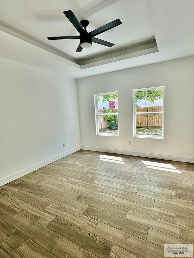 empty room with a raised ceiling, wood finished floors, baseboards, and ceiling fan