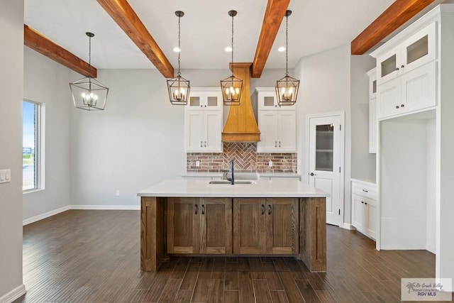 kitchen featuring sink, beam ceiling, white cabinetry, hanging light fixtures, and an island with sink