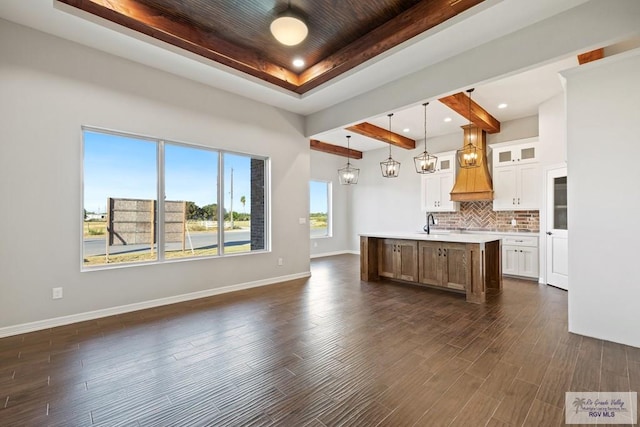 kitchen featuring a tray ceiling, dark wood-type flooring, white cabinets, hanging light fixtures, and an island with sink