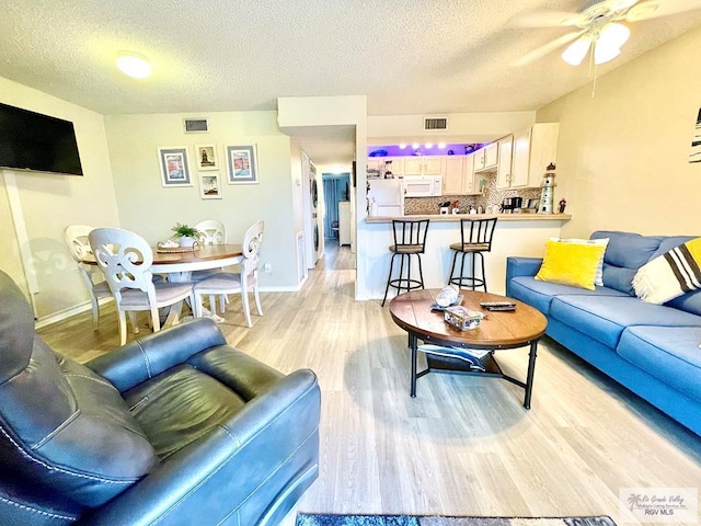 living room featuring light wood-type flooring, ceiling fan, and a textured ceiling