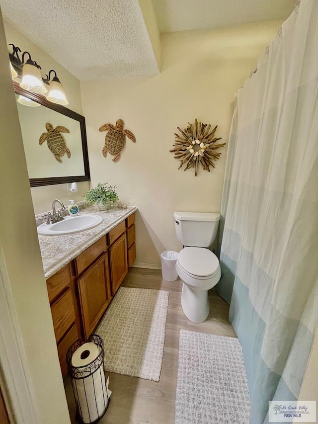 bathroom with toilet, vanity, wood-type flooring, and a textured ceiling