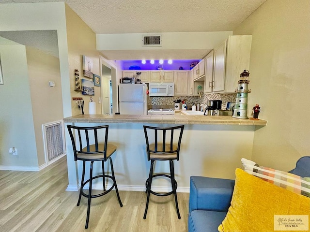 kitchen with tasteful backsplash, white appliances, light wood-type flooring, light brown cabinets, and a breakfast bar area