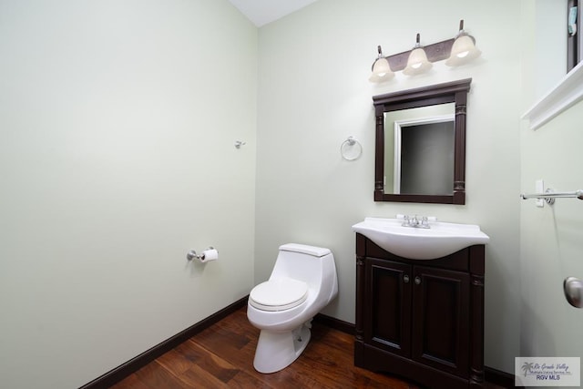 bathroom with toilet, wood finished floors, vanity, and baseboards