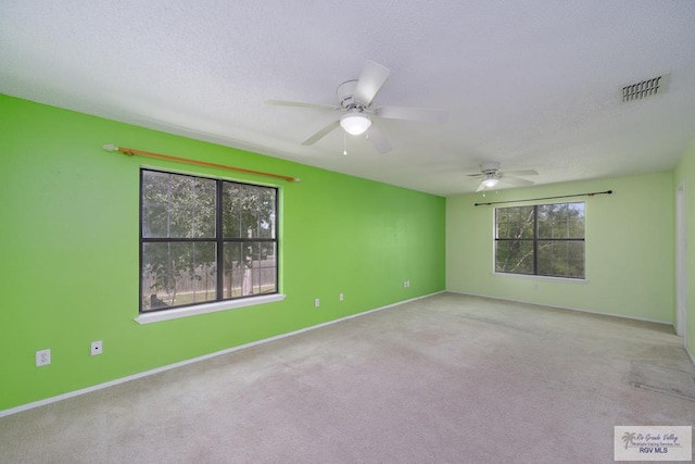 carpeted spare room with baseboards, ceiling fan, visible vents, and a textured ceiling