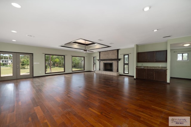 unfurnished living room with dark wood-type flooring, a fireplace, a ceiling fan, baseboards, and french doors