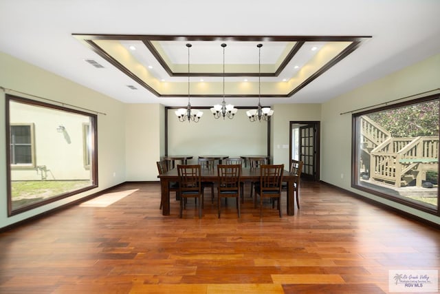 dining space featuring a raised ceiling, visible vents, baseboards, and wood finished floors