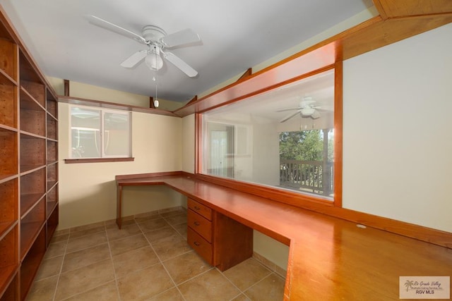 unfurnished office with a ceiling fan, built in desk, baseboards, and light tile patterned floors