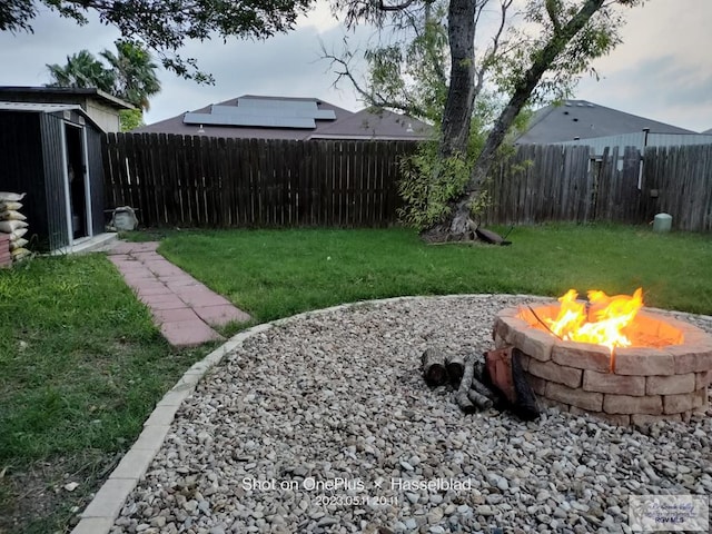 view of yard with an outdoor structure, a storage unit, a fenced backyard, and an outdoor fire pit