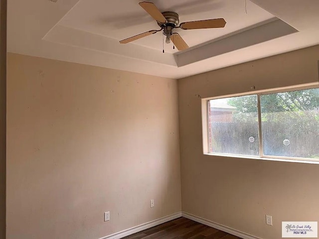 empty room featuring a tray ceiling, baseboards, dark wood-type flooring, and ceiling fan