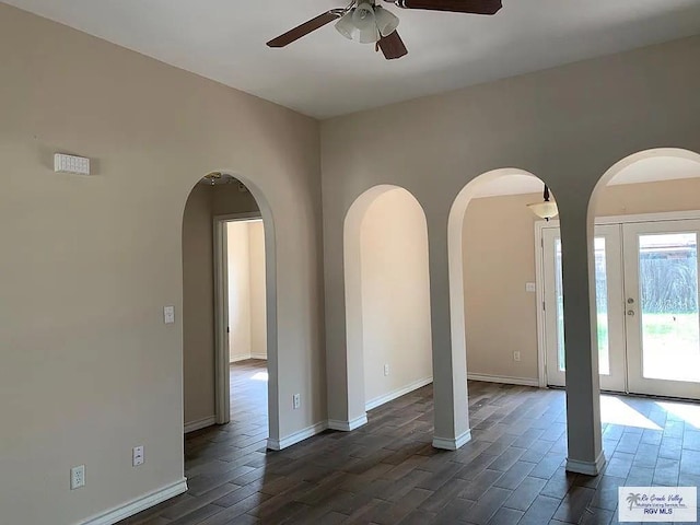 unfurnished room featuring ceiling fan, baseboards, arched walkways, and dark wood-style floors